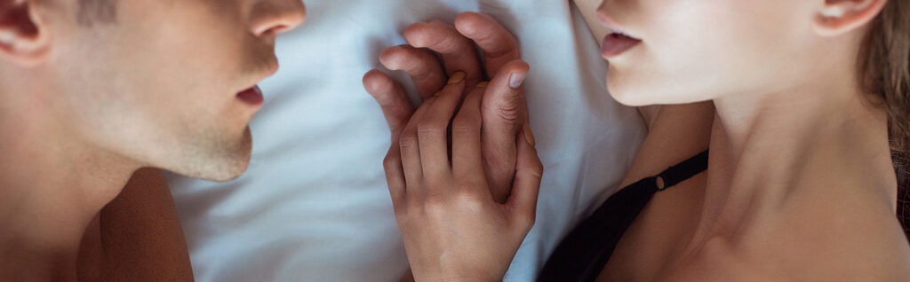 panoramic shot of man and woman lying on bed touching hands