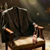 A suit jacket and tie draped over a chair, heels and a mask on the table.